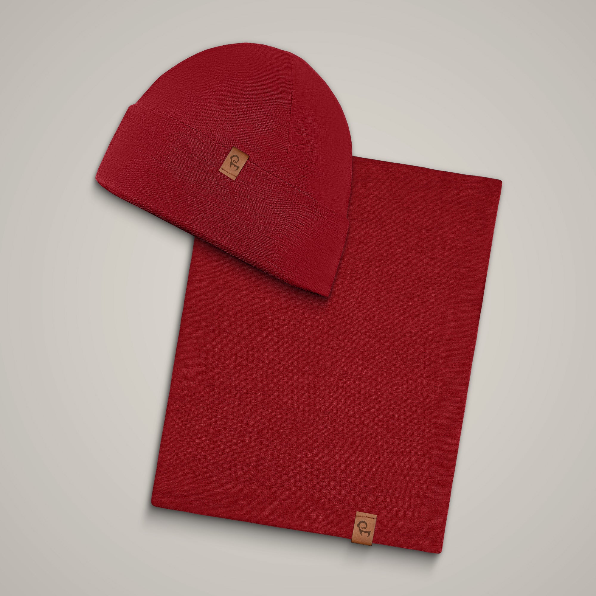 A man, standing outside in a forest during fall season, wearing the Menique Men's Merino Beanie and neck Gaiter Set in the color Royal Cherry.