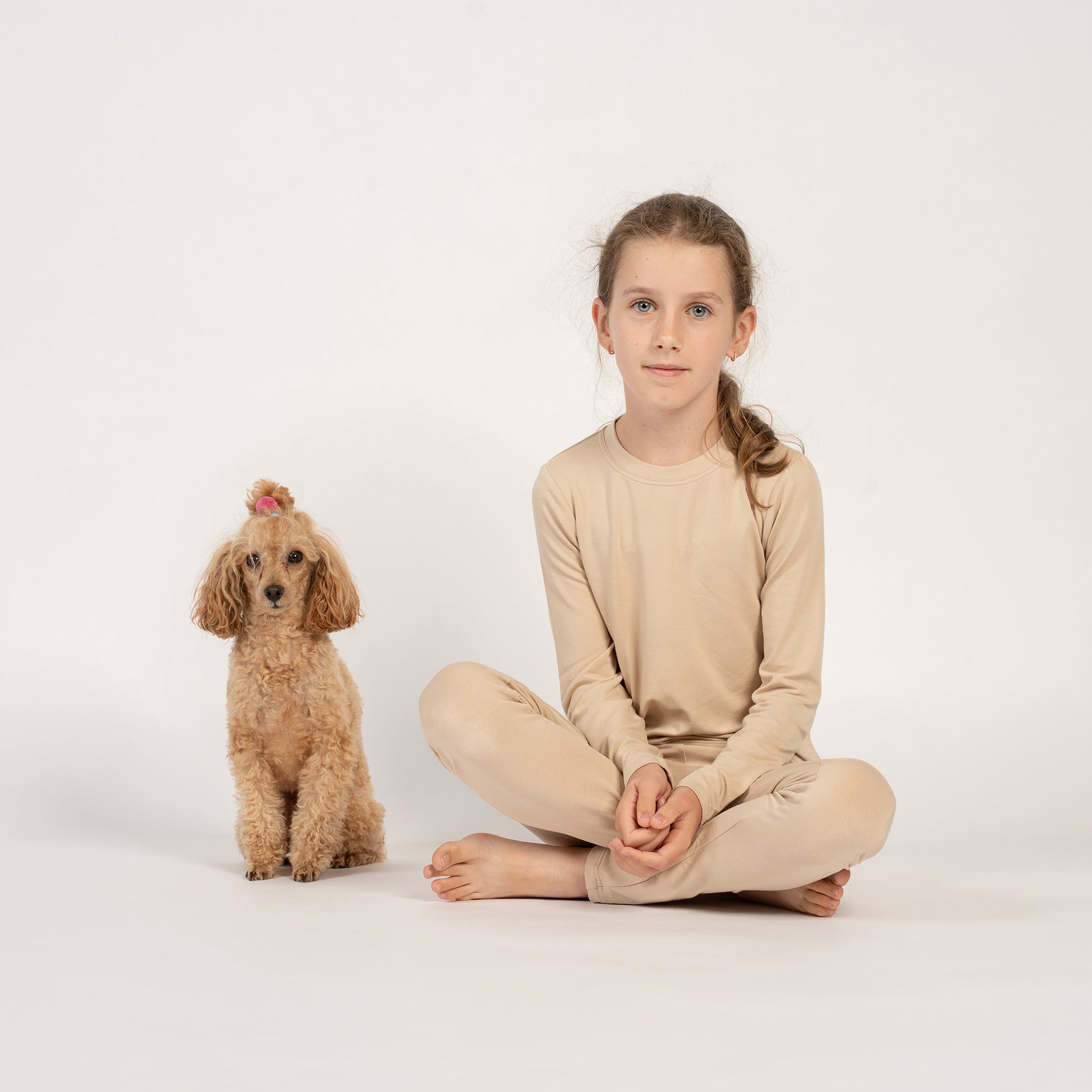 Smiling child sitting on the floor in beige bamboo long-sleeve top and bottoms.
