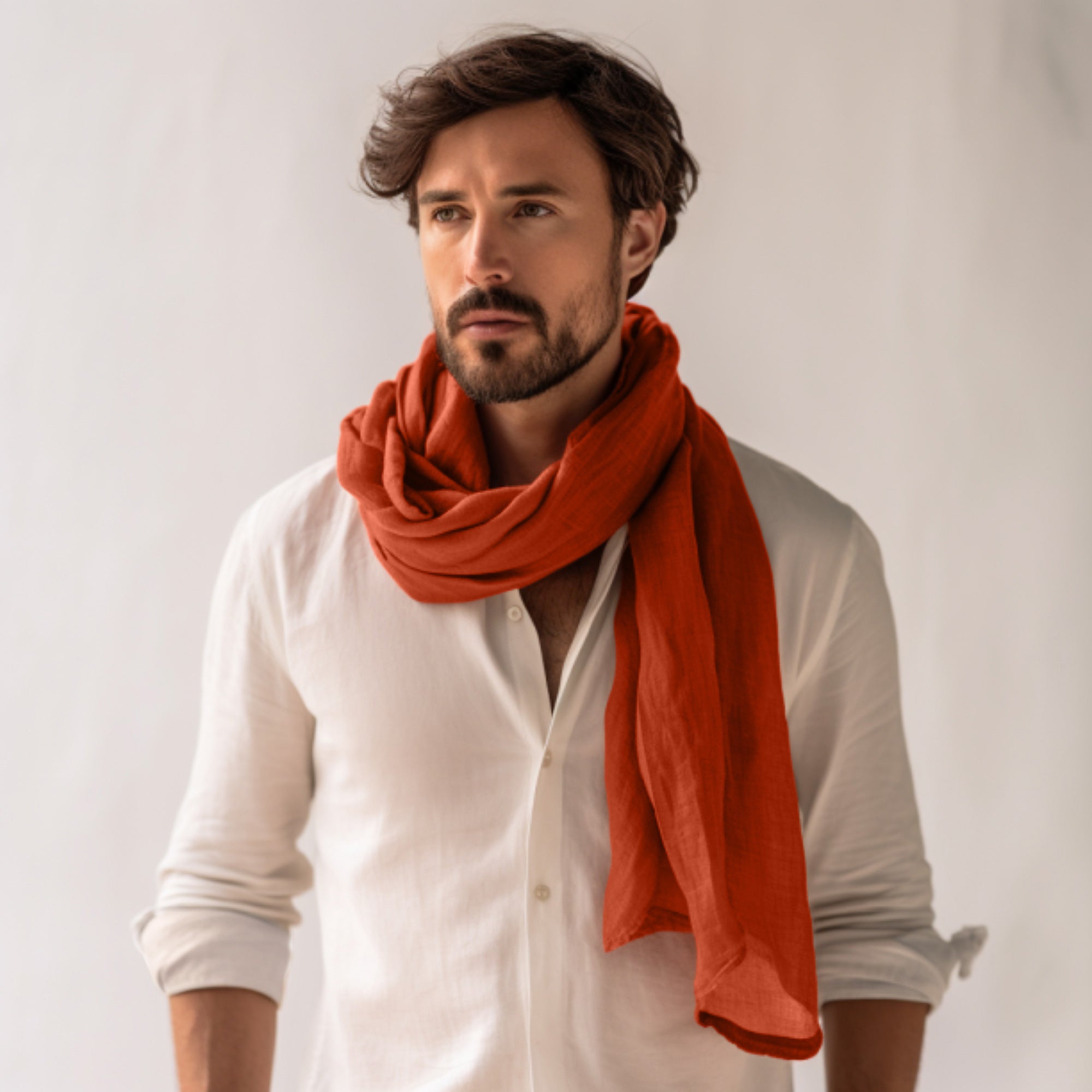 Man wearing a white shirt and orange scarf against a plain background