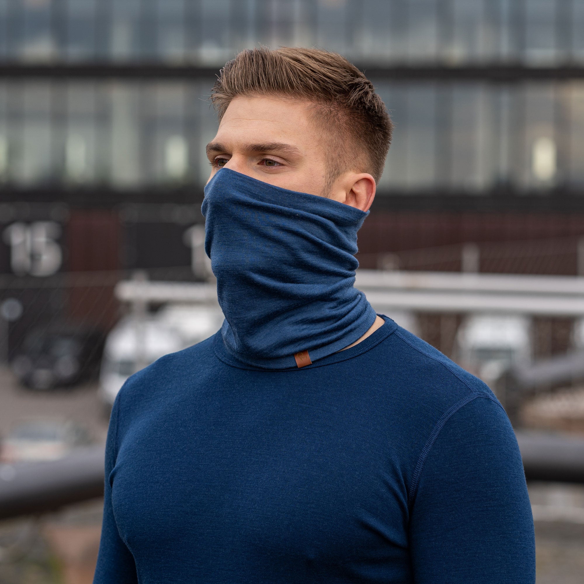 A man wearing the menique unisex denim neck gaiter. He is outside, wearing a matching color long sleeve merino top.
